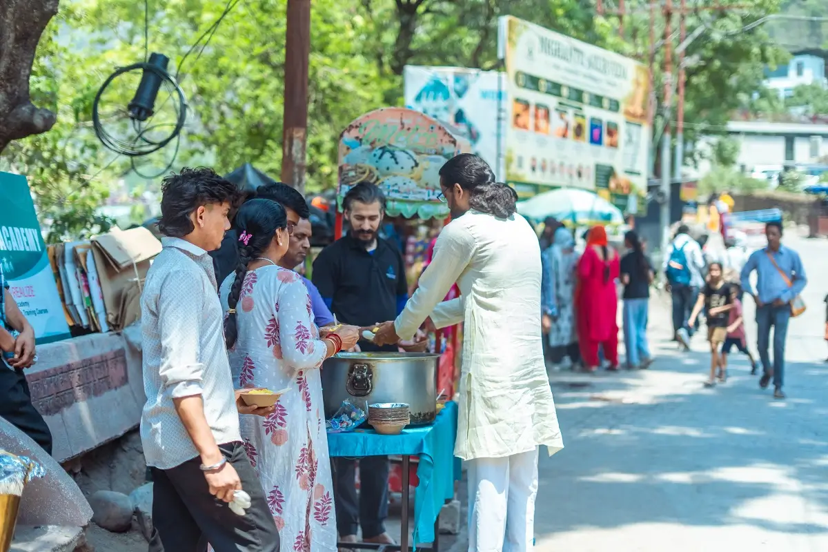Volunteers ladling food from a large pot into bowls at the roadside stall in Rishikesh