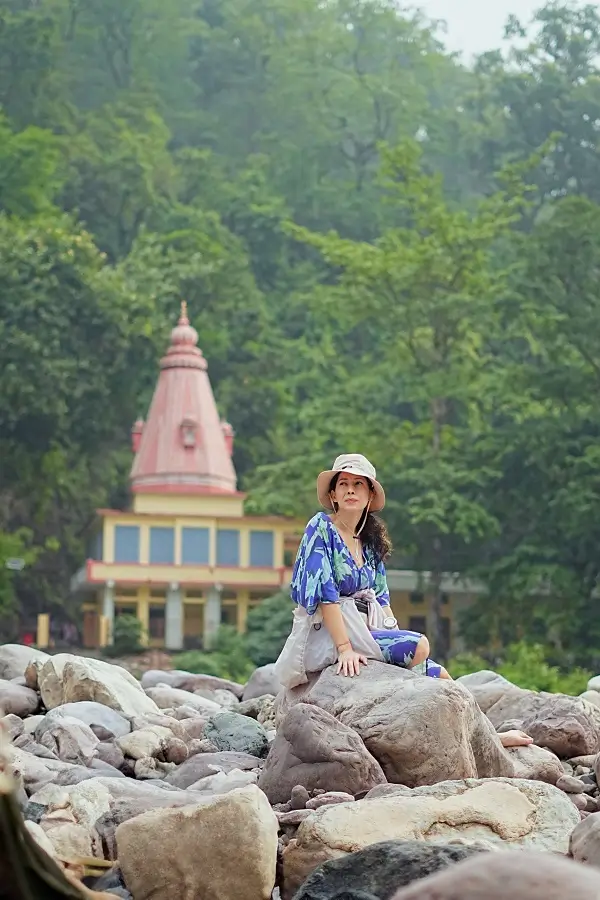 Student holding camel pose on the sand at the riverbank, boulders behind
